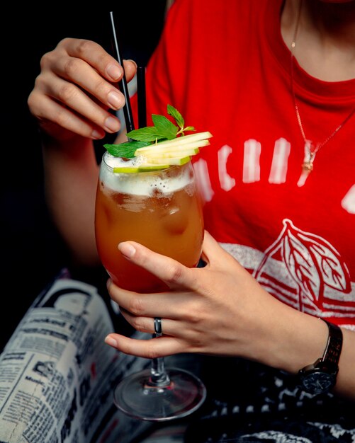 Mujer sosteniendo una copa de cóctel de naranja con rodajas de manzana verde