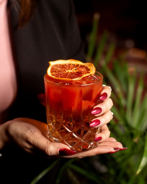 Mujer sosteniendo una copa de cóctel rojo adornado con rodaja de naranja seca