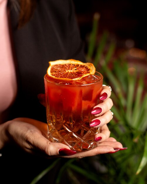 Mujer sosteniendo una copa de cóctel rojo adornado con rodaja de naranja seca