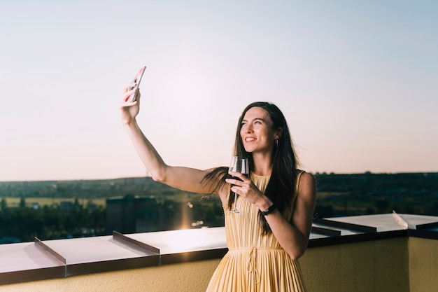 Mujer sosteniendo una copa de vino y tomando selfie en la azotea