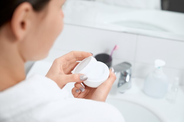 Mujer sosteniendo crema facial o corporal en el baño.