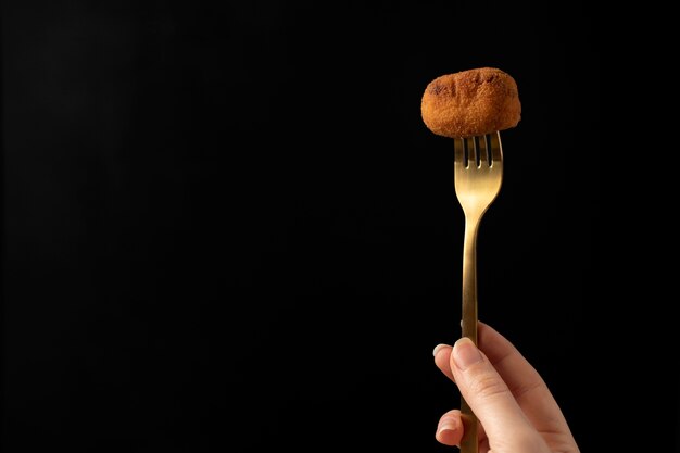 Mujer sosteniendo una croqueta con un tenedor dorado