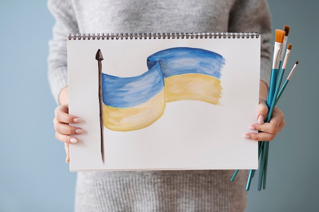 Mujer sosteniendo cuaderno con dibujo de bandera ucraniana