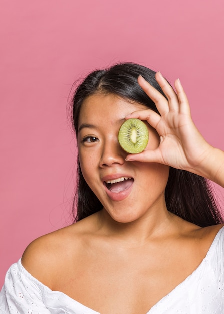 Mujer sosteniendo y cubriendo un ojo con kiwi