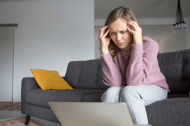 Mujer sosteniendo los dedos en los templos, mirando portátil en la mesa