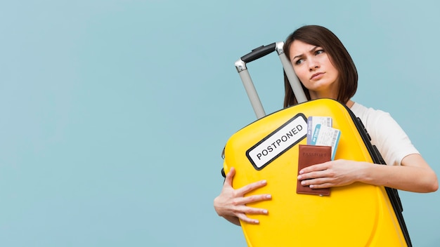 Mujer sosteniendo un equipaje amarillo con un cartel pospuesto con espacio de copia