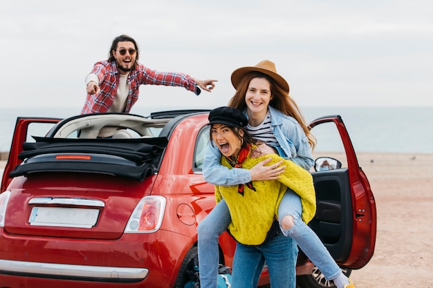 Mujer sosteniendo en la espalda feliz dama cerca de hombre inclinado hacia fuera del coche