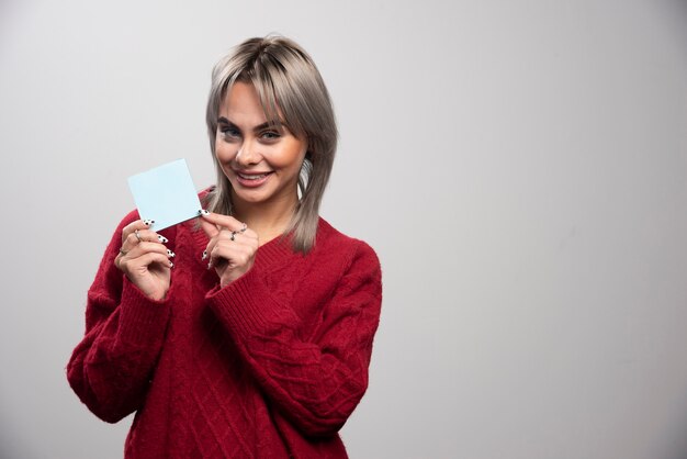 Mujer sosteniendo felizmente el bloc de notas sobre fondo gris.