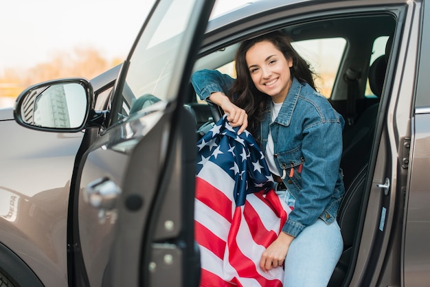 Mujer sosteniendo gran bandera de Estados Unidos en coche