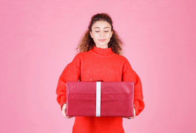 mujer sosteniendo una gran caja de regalo roja.