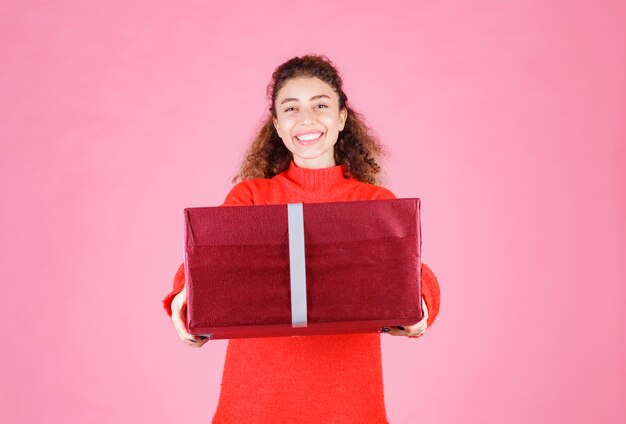 mujer sosteniendo una gran caja de regalo roja.