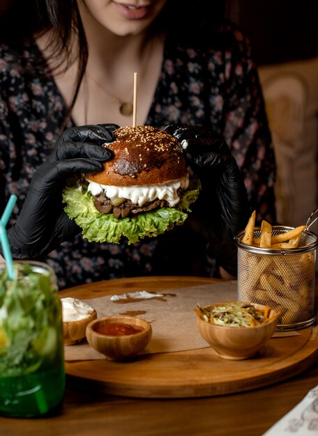 Mujer sosteniendo con guantes negros hamburguesa de ternera con champiñones, lechuga y queso