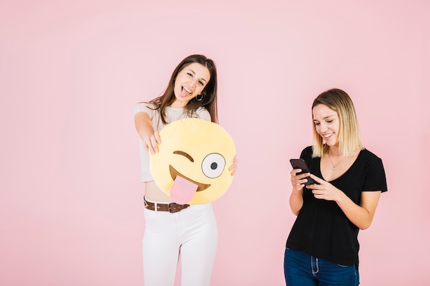 Mujer sosteniendo guiñando ojo emoji cerca de su amigo usando teléfono celular