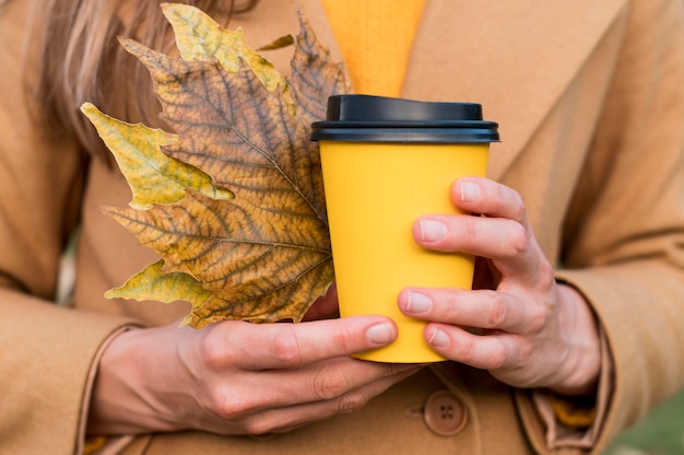 Mujer sosteniendo hojas de otoño y una taza de café