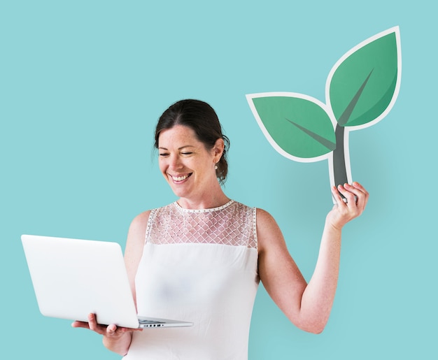 Mujer sosteniendo un icono de planta y usando una laptop