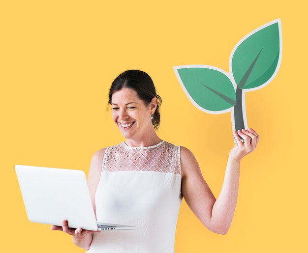 Mujer sosteniendo un icono de planta y usando una laptop