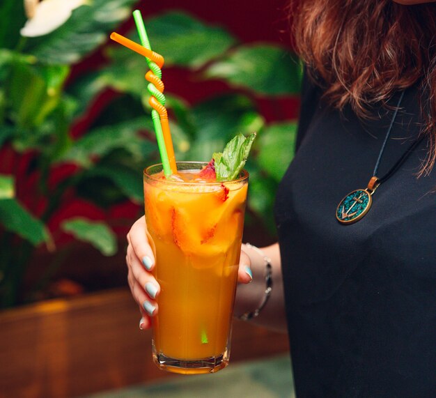 mujer sosteniendo jugo de naranja con rodajas de fresa y naranja