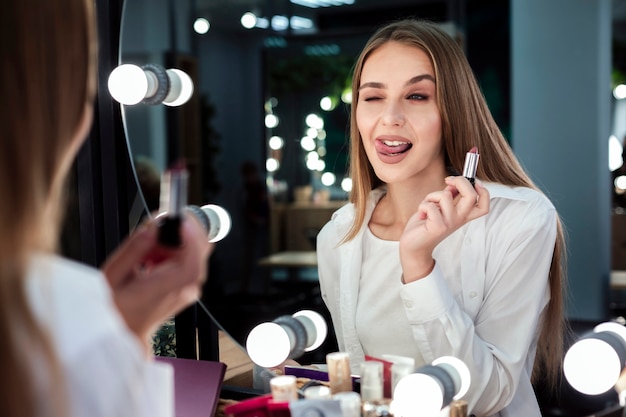 Foto gratuita mujer sosteniendo el lápiz labial mirando al espejo