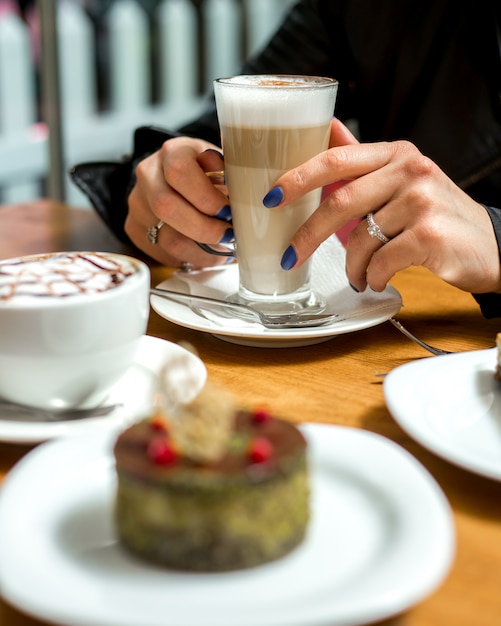 Una mujer sosteniendo latte machiato con postre sobre la mesa