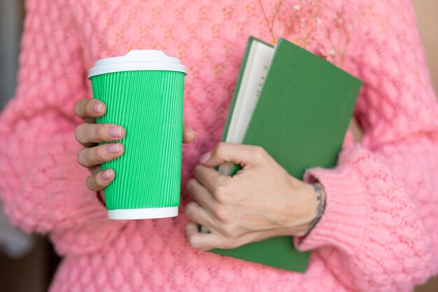 Mujer sosteniendo un libro abierto con un ramo de flores secas en el interior y una taza de café de papel