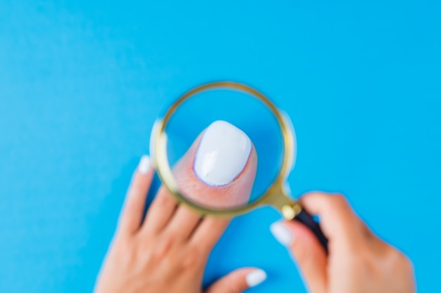 Mujer sosteniendo lupa sobre uñas