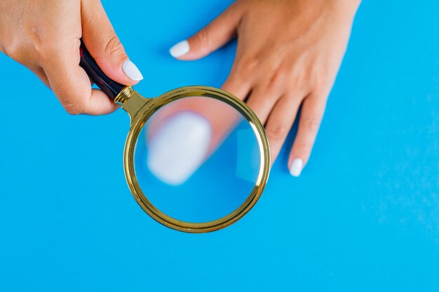 Mujer sosteniendo lupa sobre uñas