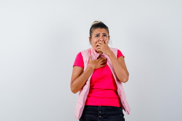 Mujer sosteniendo la mano en la boca en camiseta, chaleco y mirando melancólica