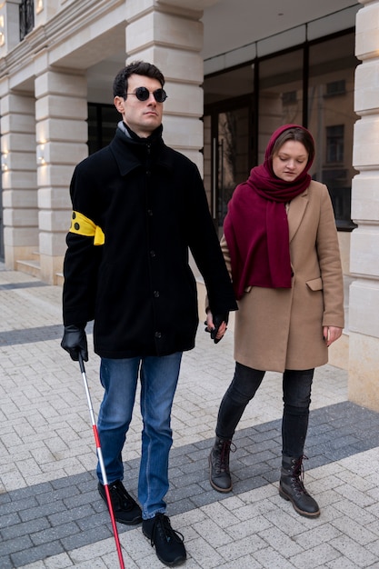 Mujer sosteniendo la mano de un ciego para ayudarlo a caminar