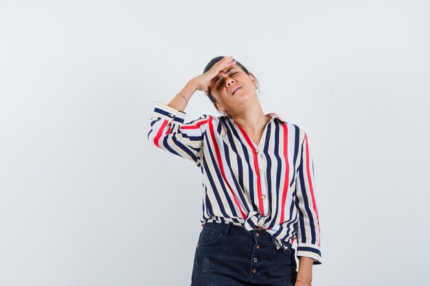 mujer sosteniendo la mano sobre los ojos en camisa, falda y con aspecto cansado.