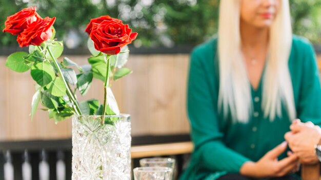 Mujer sosteniendo la mano de su novio frente a hermosas tres rosas rojas en el florero