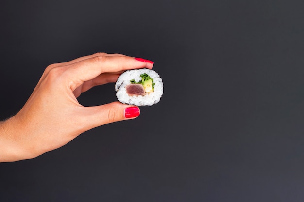 Mujer sosteniendo en la mano un trozo de sushi roll