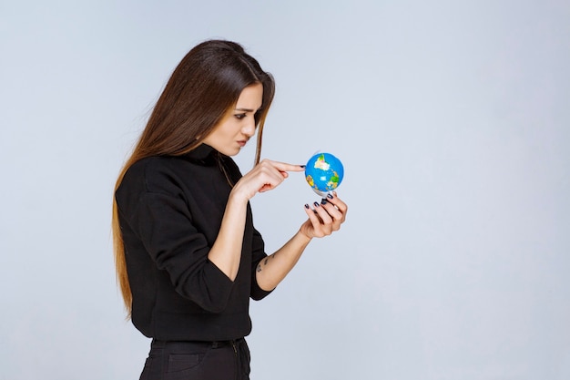 mujer sosteniendo un mini globo y encontrando ubicaciones en él.