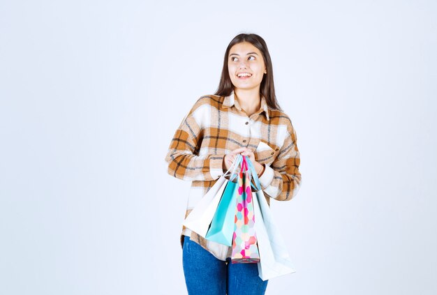 mujer sosteniendo un montón de bolsas de la compra sobre la pared blanca.