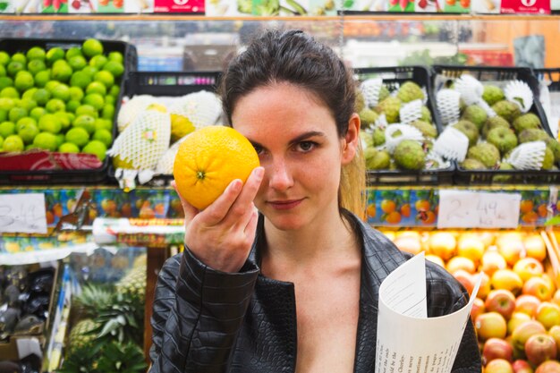 Mujer sosteniendo una naranja en una tienda de comestibles