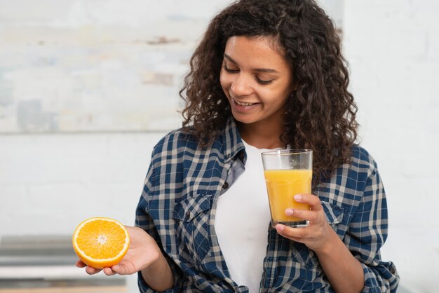 Mujer sosteniendo una naranja y un vaso de jugo