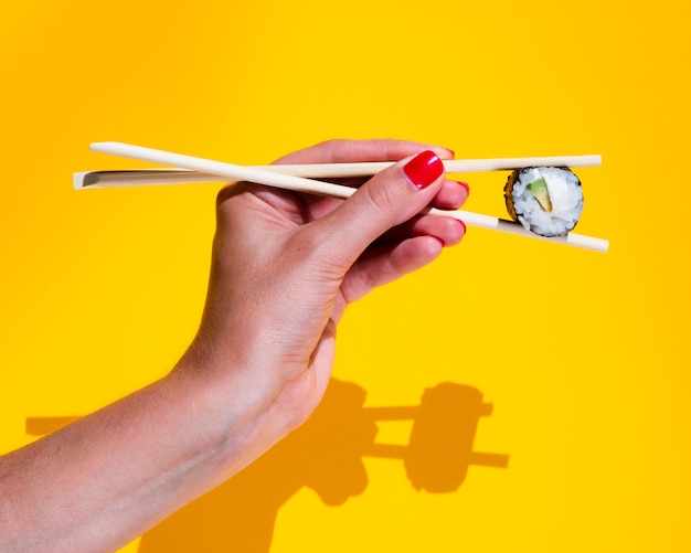 Mujer sosteniendo un nigiri sobre un fondo amarillo