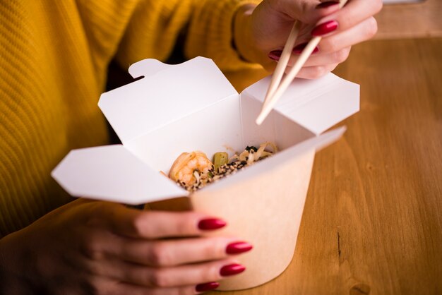 Mujer sosteniendo palillos y caja de fideos