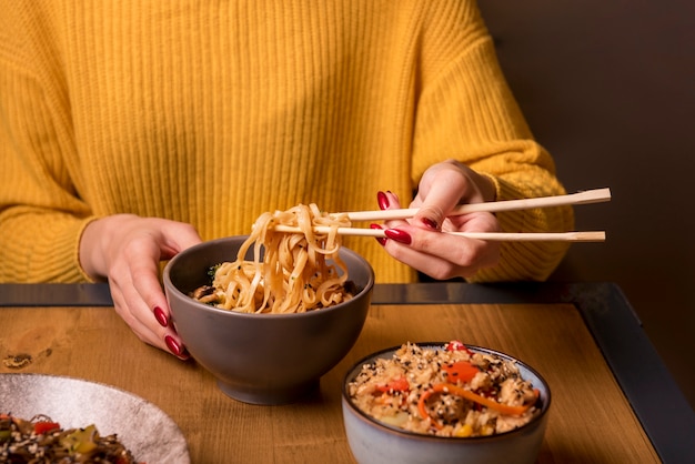 Mujer sosteniendo palillos con fideos en la mesa