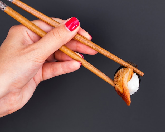 Mujer sosteniendo en palillos de madera un sushi