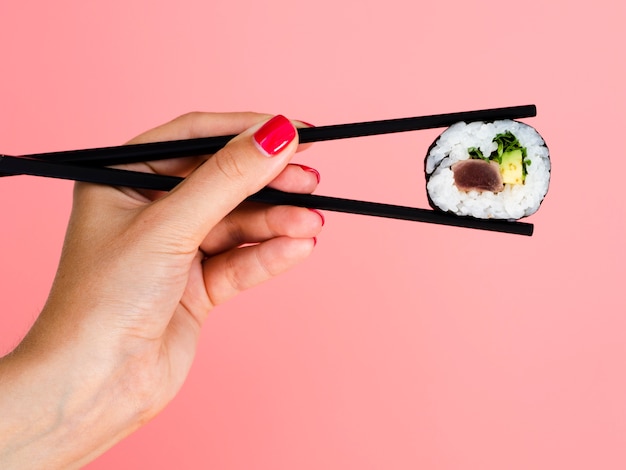 Mujer sosteniendo en palillos un rollo de sushi sobre un fondo rosa