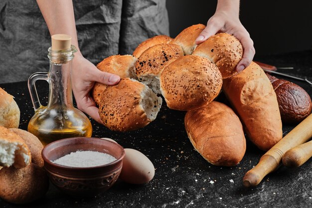 Mujer sosteniendo pan sobre mesa oscura con huevos, tazón de harina y vaso de aceite.