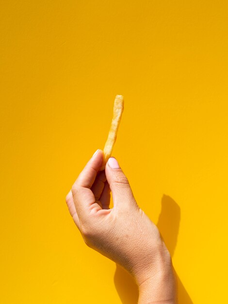 Mujer sosteniendo papas fritas delante de fondo amarillo