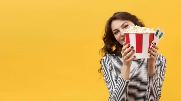 Mujer sosteniendo un par de gafas 3d y un cubo con palomitas de maíz