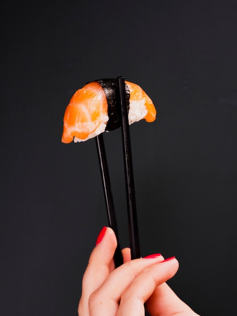 Mujer sosteniendo un par de palillos con sushi de salmón