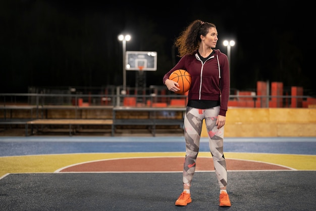 Mujer sosteniendo la pelota de baloncesto al aire libre full shot