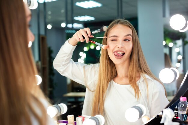 Mujer sosteniendo pinceles de maquillaje haciendo cara graciosa