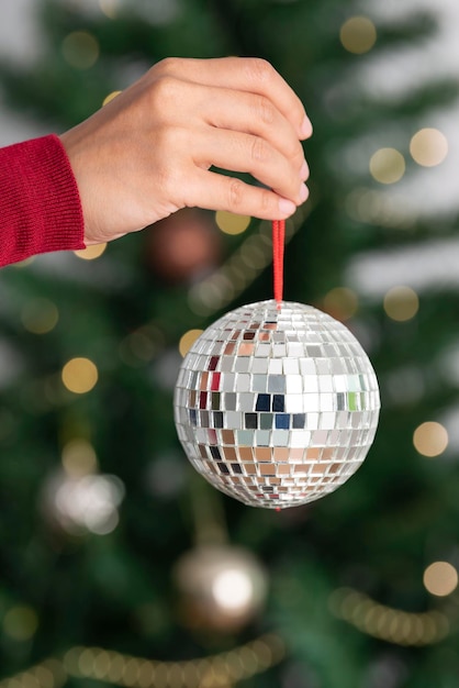 Foto gratuita mujer sosteniendo plata bola de discoteca de navidad sobre fondo de árbol de navidad