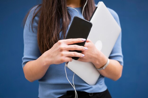 Mujer sosteniendo portátil y teléfono inteligente con auriculares