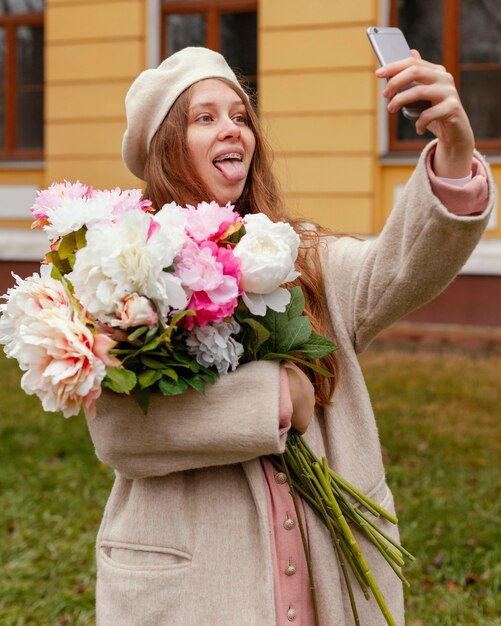 Mujer sosteniendo ramo de flores al aire libre en la primavera y tomando selfie