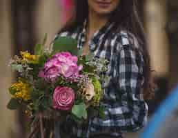 Foto gratuita una mujer sosteniendo un ramo de flores mixtas en tonos de rosa en la mano en una vista de la calle